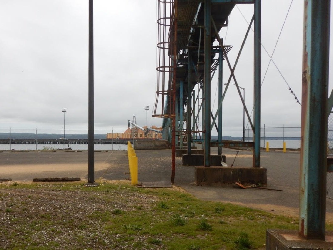 Conveyor gantry at a waterfront loading facility, with a barge of wood chips beyond